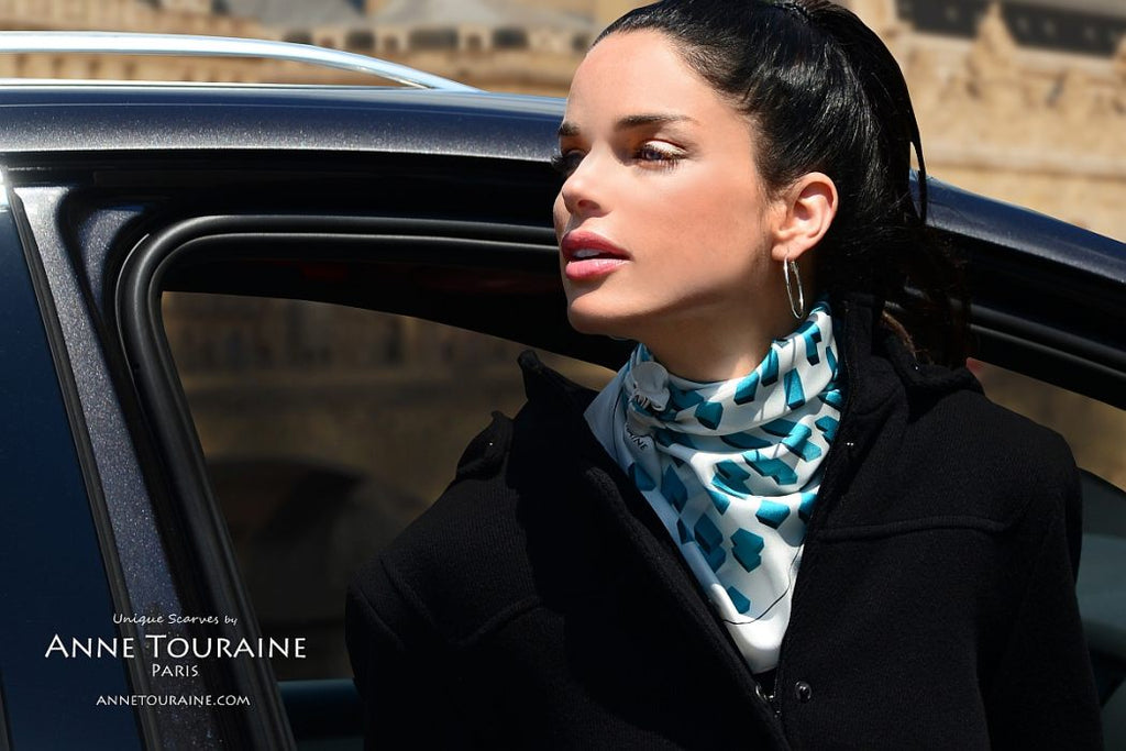 French silk scarves by ANNE TOURAINE Paris™: Teal and white geometric scarf tied as kerchief over a coat and slightly tilted to the side of the neck