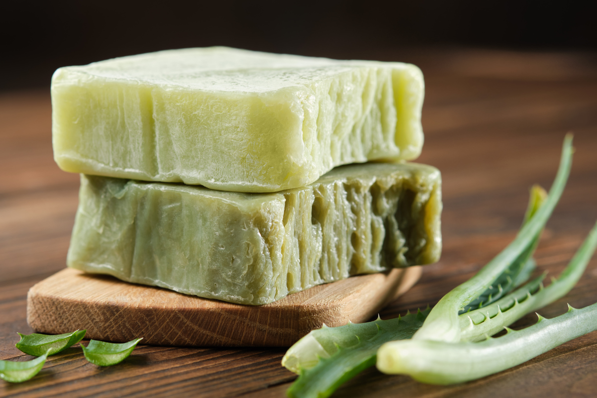 "A hand-made piece of natural soap: a blend of fragrant essential oils and natural ingredients for gentle cleansing and care of the skin. Green with aloe vera on a wooden background."