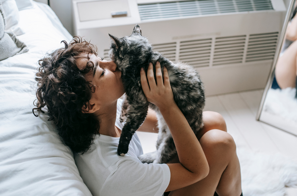 Beautiful brown-haired woman kissing her calico cat.