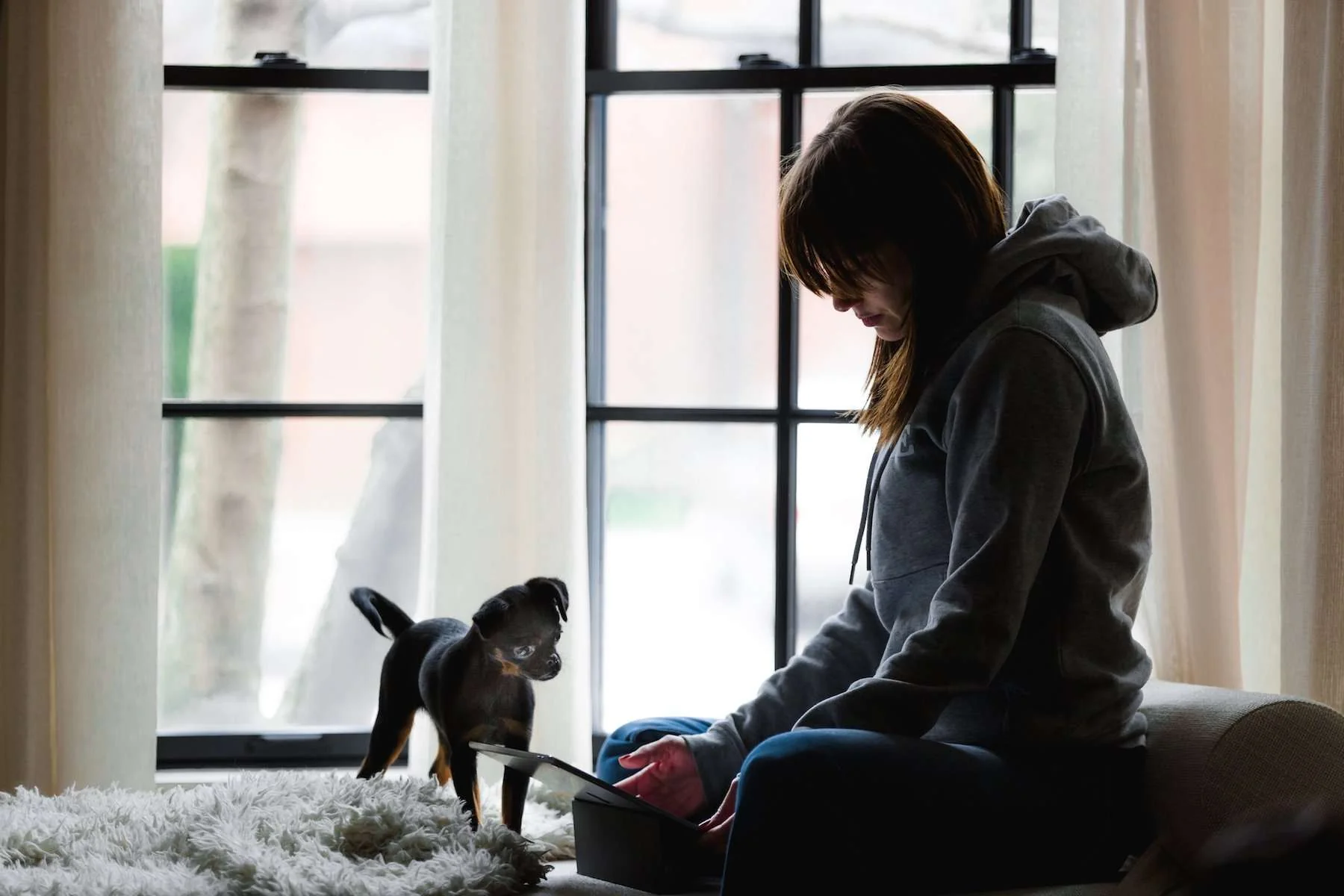 Muchacha sentada en la cama leyendo su tablet junto a su perro