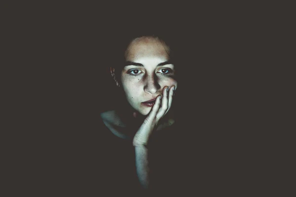 Unsplash-Mujer con cara apoyada sober mano en fondo oscuro