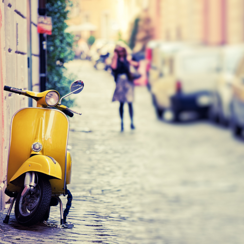 A yelloiw vespa parked on an Italian streed