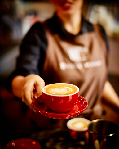 a woman serving Dello Mano Coffee in a red cup