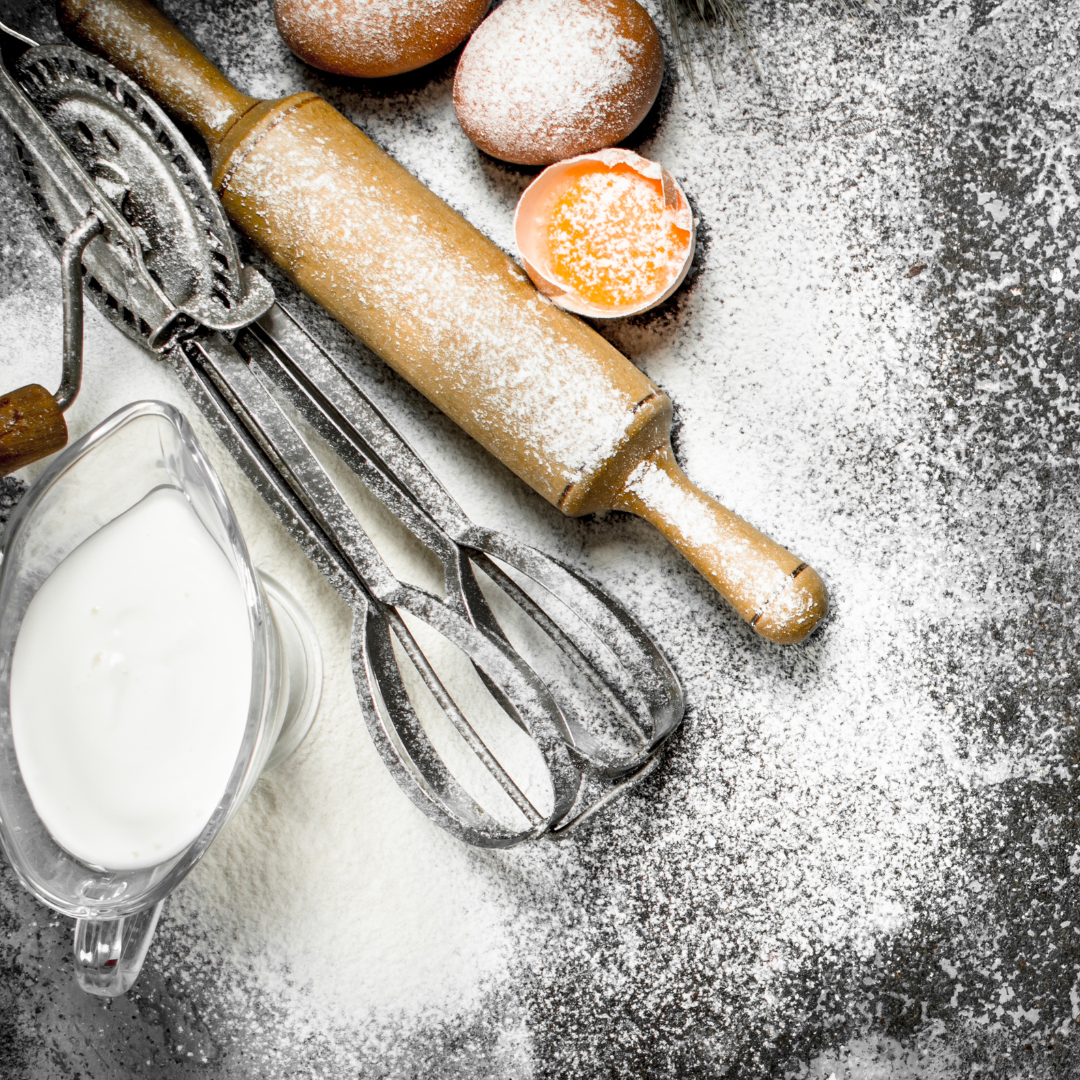 Baking Tools a whisk and rolling pin with eggs and milk on a board.