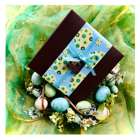 An Easter Gift box finished with blue and green wrap sitting on a wreath of coloured easter eggs.