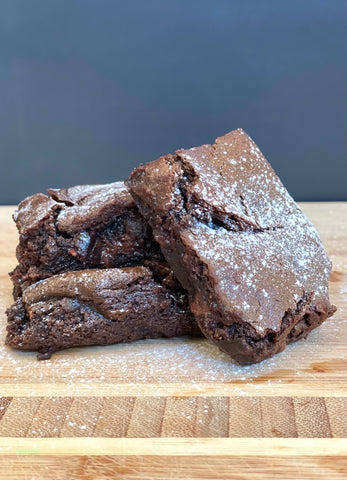 Vegan gluten-free tahini brownies with icing sugar dusting displayed on a wood surface