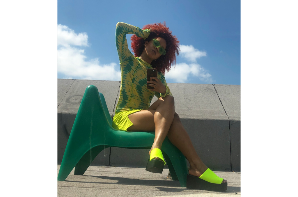 Model with red hair sitting in green chair wearing Colette lime green skirt with lime and teal top.