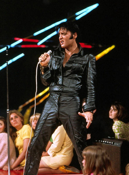 Elvis Presley on stage wearing a black leather shirt and pants.