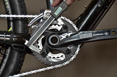 Caliper measuring distance between opposing bolts on chainring on bicycle