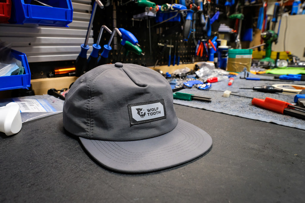 A Wolf Tooth Nylon Patch Hat sits on a workbench surrounded by bike tools.