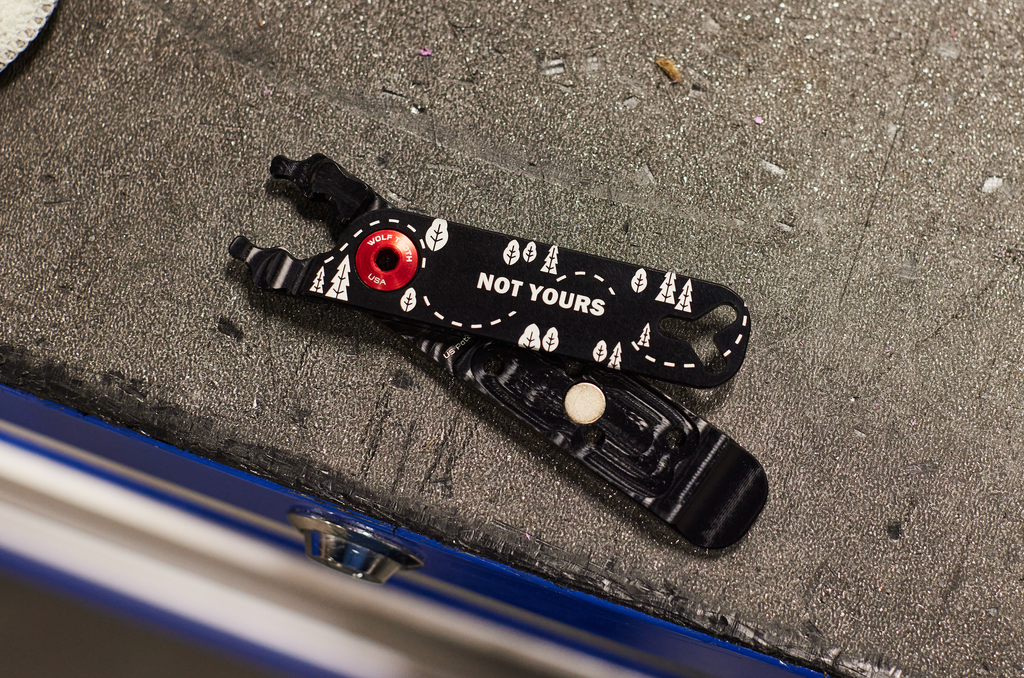 A pair of custom laser engraved Wolf Tooth Pack Pliers are lying on a workbench. The Pack Pliers say "Not Yours."