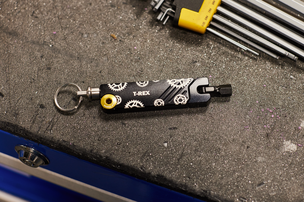 A custom laser engraved Wolf Tooth 6-Bit Hex Wrench Multi-Tool is on a workbench. The custom laser engraving says "T-Rex."