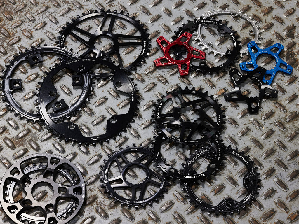 A collection of Wolf Tooth chainrings, including CAMO Spiders and rings, chainrings for Shimano GRX, SRAM Direct Mount, 130 BCD Elliptical, CAMO Bash Ring, and chainrings for Race Face.