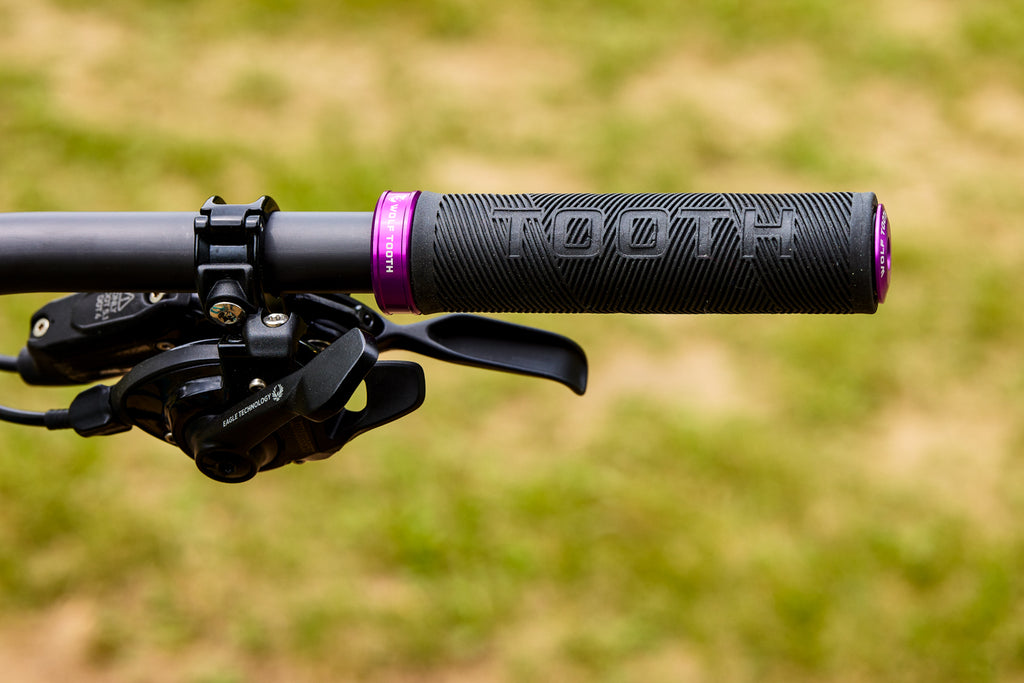 A Wolf Tooth Echo Lock-On Grip is secured to the handlebars of an Ibis mountain bike. Two hands are shown pulling the Wolf Tooth EnCase System Bar Kit One out from inside of the grip. 