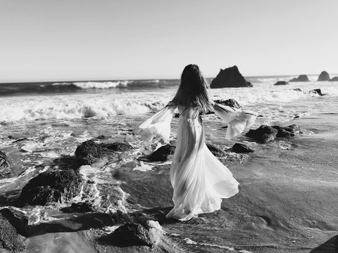 Fashion Designer Lauren Elaine twirls in a bell-sleeve off-the-shoulder wedding gown at el matador state beach in Malibu, California