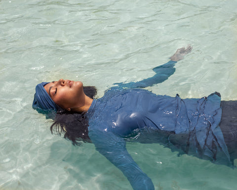 A woman floating in the sea wearing Lanuuk Lula swimwear in Azure and a matching Azure swim turban.