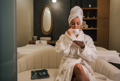 Woman at a spa wearing a robe and sitting on a sofa drinking from a mug