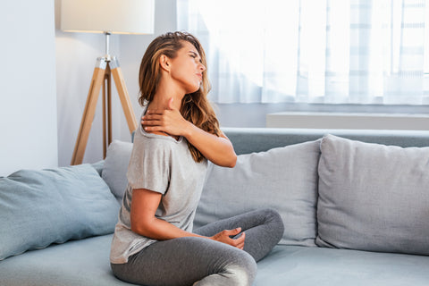 Woman sitting on couch clutching shoulder in pain. 