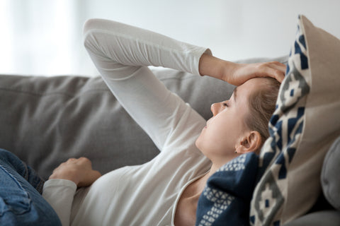 Woman lying on couch with hand to head because of chronic headache