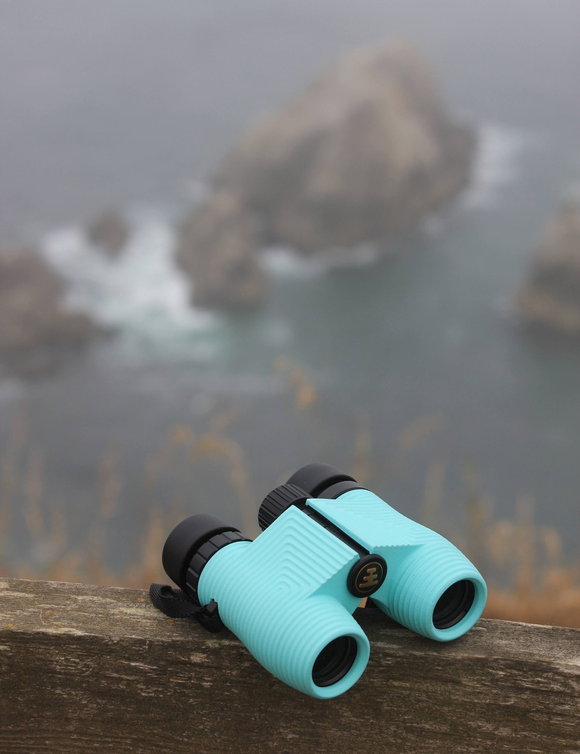 Nocs compact fogproof and waterproof binoculars propped up on a cliff overlooking the ocean