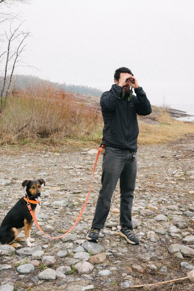 Daniel Schechner holding the leash for his dog, while looking through nocs standard issue 8x25 binoculars
