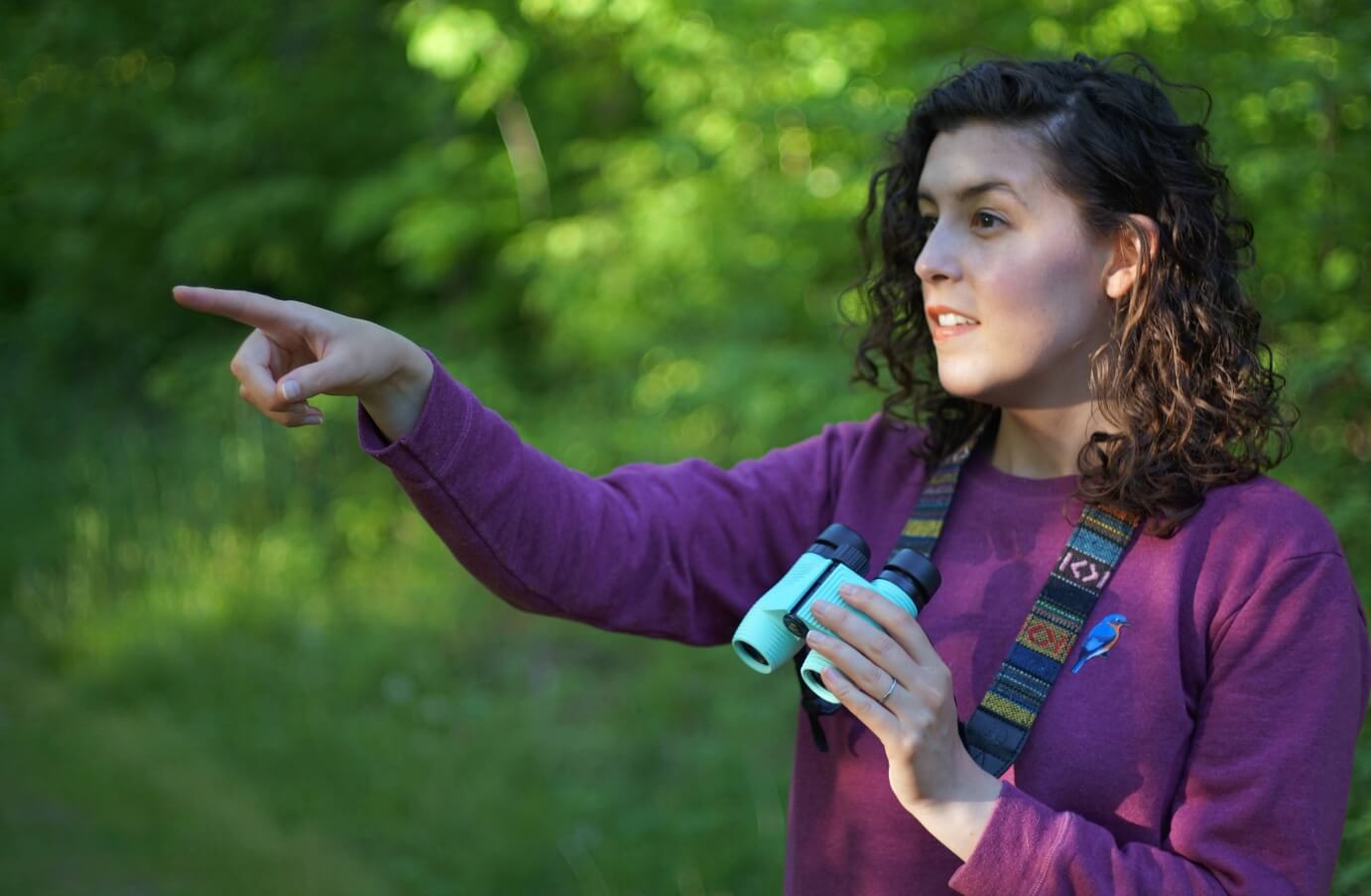 Emily Piper pointing something out in the distance on a hike, holding a pair of Nocs standard issue 8x25 binoculars