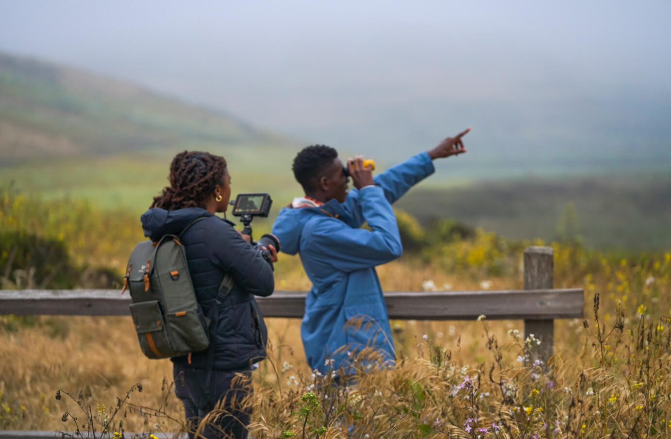 A picture of Isaiah Scott and a friend on a hiking trail, looking through a pair of Nocs and pointing out something in the distance