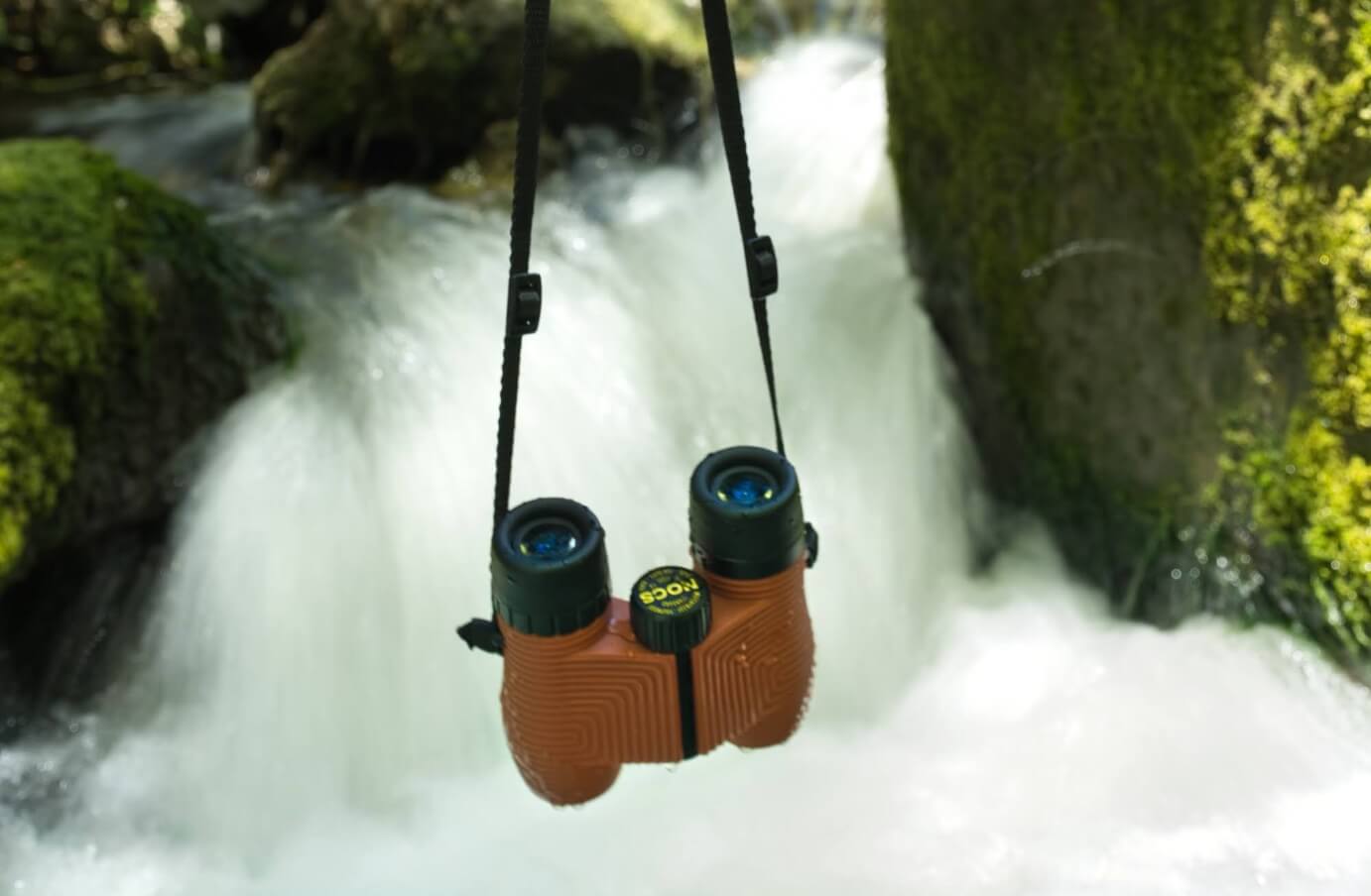 a pair of Nocs being held in front of a flowing waterfall