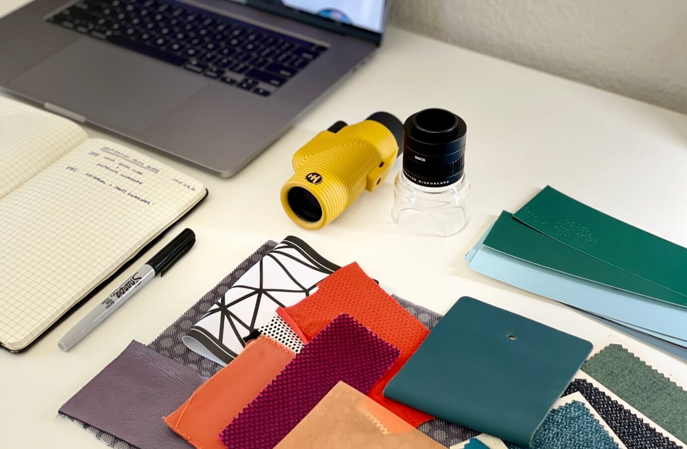 items on a desk arranged nicely: a laptop, a nocs monocular, a notebook, scrap paper