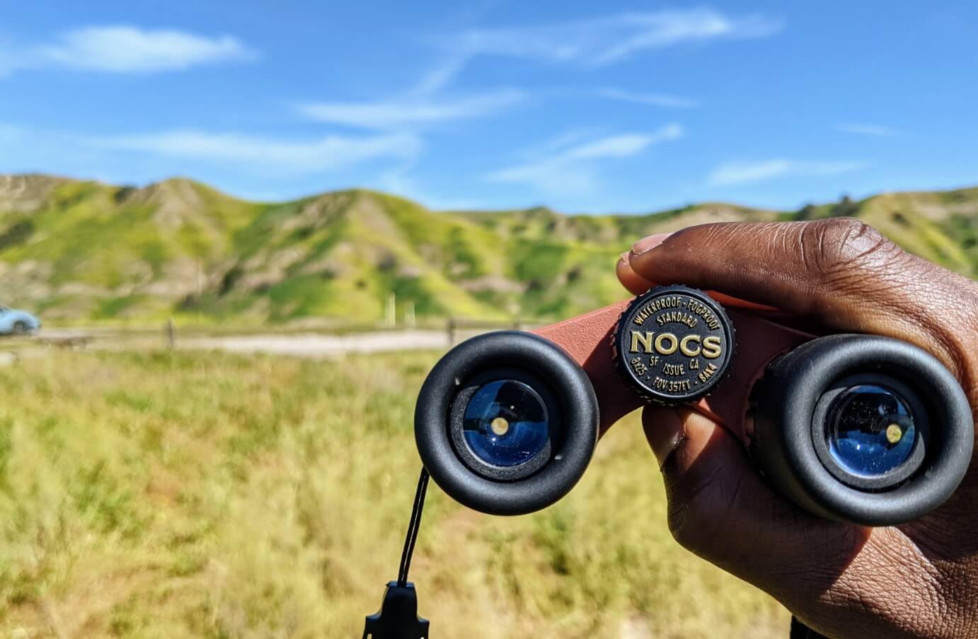 Close up picture of a pair of Nocs being held, with grass hills in the distance