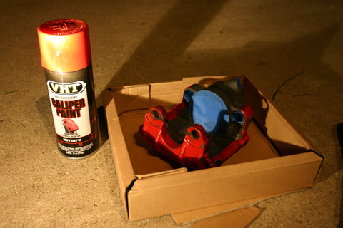 Brake caliper masked with blue painters tape and a can of very high temperature spray paint next to it.