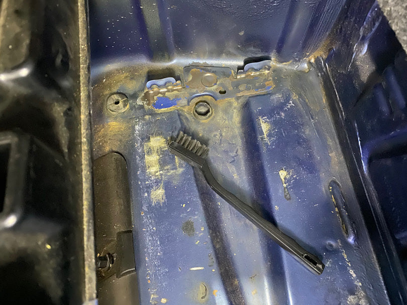 BMW E36 battery compartment after scrubbing rust with a stainless steel brush about the size of a toothbrush. Rusty areas are now dull metal.