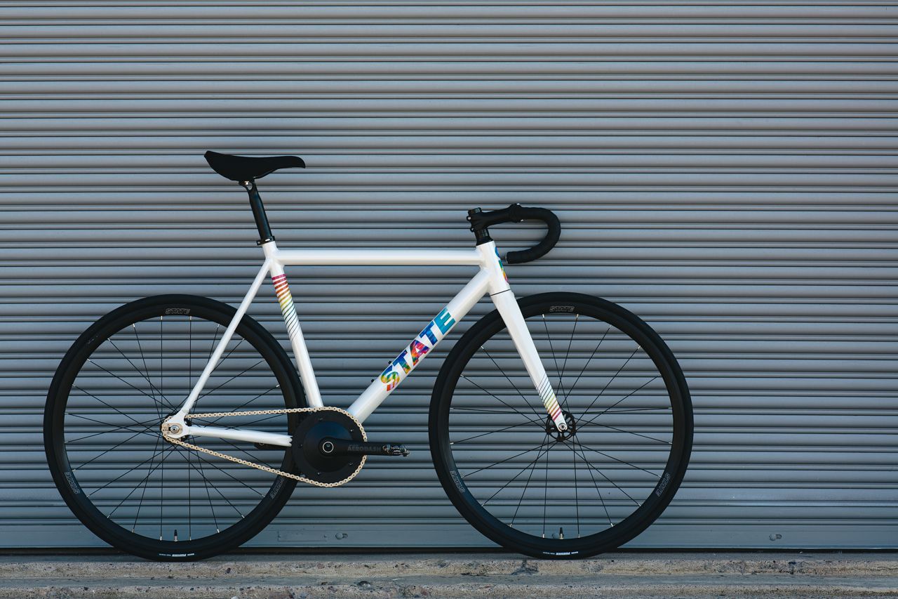  A white with rainbow font bicycle leaned against a wall