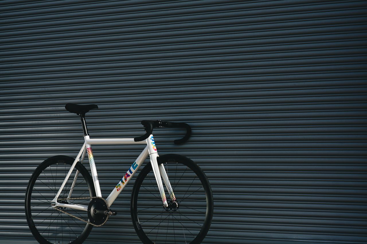  A white with rainbow font bicycle leaned against a wall
