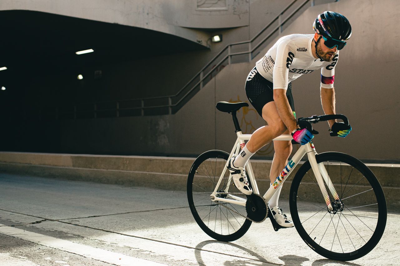 A cyclist riding a white with rainbow font bicycle on the road