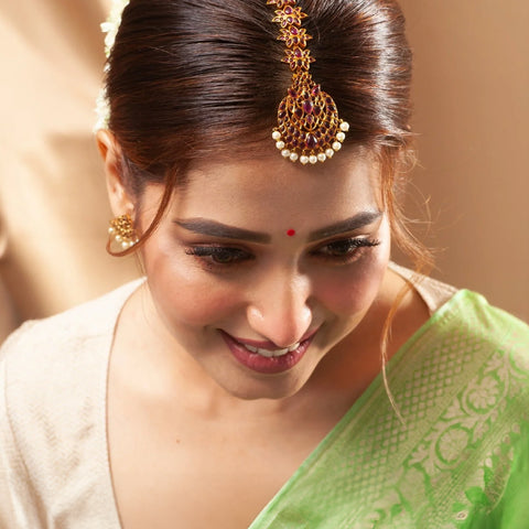 An image of a woman showcasing a maang tikka with a green saree and a gajra in her bun