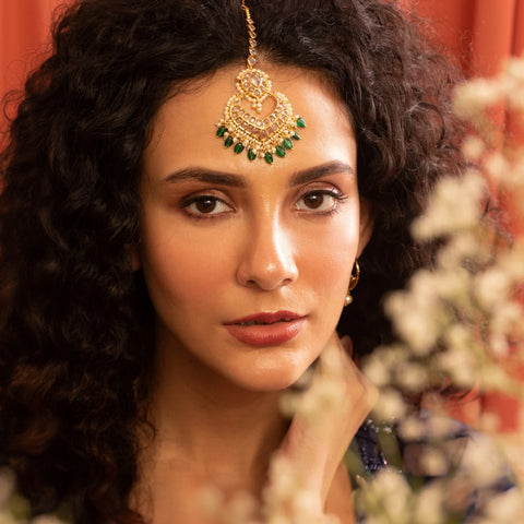An image of a woman showcasing a maang tikka while styling it with curly hair