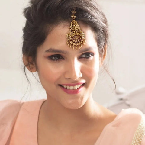 A picture of a woman wearing a maang tikka with a side swept bun