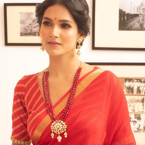 An image of a woman wearing a red saree with an Indian kundan necklace.