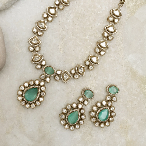 An image of a short necklace, crafted with Polki stones and green gemstones on a beige background