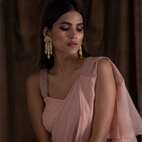 An image of a woman wearing a pink saree with a stylish pair of drop earrings