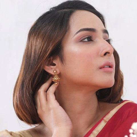 An image of a woman wearing red saree while showcasing an antique earrings in her ear