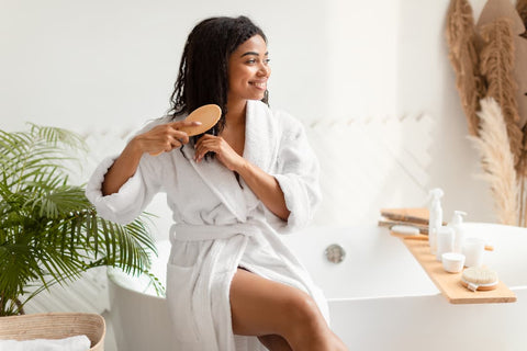 Femme en peignoir blanc dans sa salle de bain qui se brosse les cheveux avec une brosse à cheveux