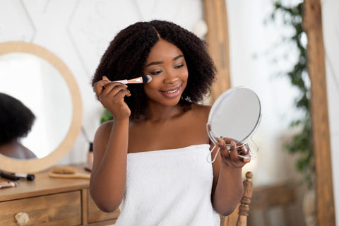 Femme se maquillant face à un miroir de poche avec cheveux bouclés et soins aux probiotiques
