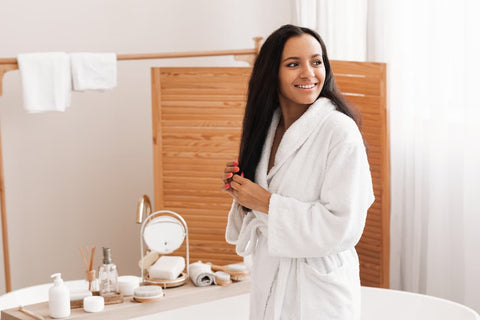 Femme qui se brosse les cheveux en peignoir dans sa salle de bain avec une brosse à cheveux