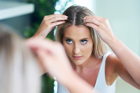 Femme qui regarde son cuir chevelu avec des pellicules avant d'utiliser le shampooing antipelliculaire