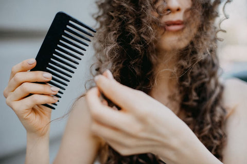 Femme se brosse les cheveux bouclés avec une brosse lissante