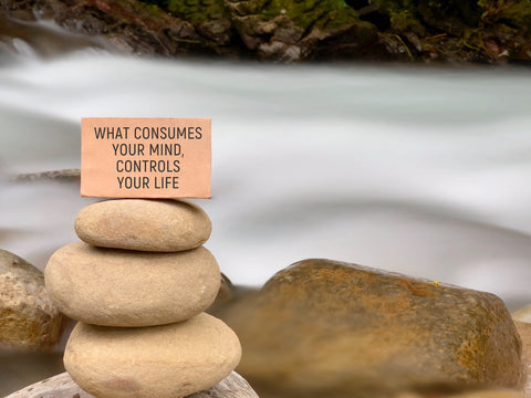 what consumes your mind, controls your life written on a board that is sitting on top of 3 stacked rocks