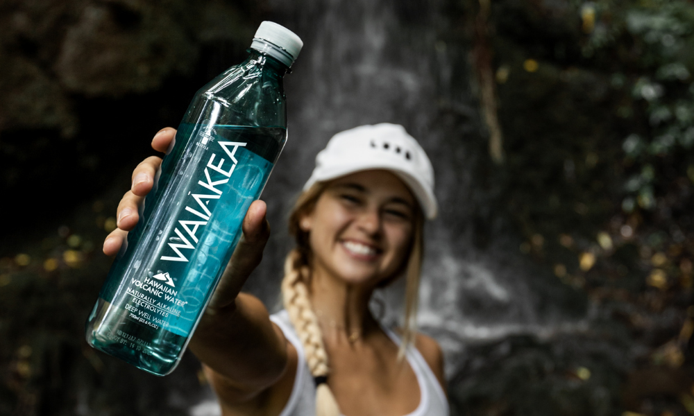 woman holding an Oceanplast®  waterbottle in front of a waterfall