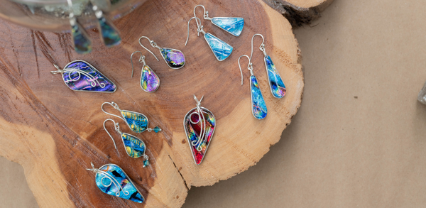 Image of dichroic glass earrings and pendants on a wood slab. All our nickel free.